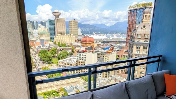 A balcony with a grey sofa and a view of a cityscape. - Modern DT 2-Bed Condo, Large Balcony, Great View, Free Parking, A/C, EV charger (Vancouver)