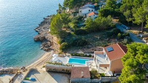 Vue aérienne d’une propriété située sur la côte, avec une piscine, une plage et un rivage rocheux.