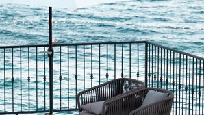 Un balcon avec vue sur la mer, comprenant une table avec des éléments pour le petit-déjeuner et deux chaises en osier.