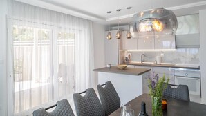 A modern kitchen with pendant lighting, a dining area with a table and chairs, and a view through large windows. - Villa Noemi by MyWaycation (Sumartin)