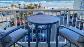 A balcony with a view of the ocean, a table, and two chairs. - NEW Amazing Ocean Front King Bed Studio in Daytona! (Daytona Beach)