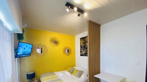 Une chambre d’hôtel de taille réduite, comprenant un lit, un bureau, une chaise et un téléviseur fixé au mur.