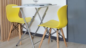 Une petite pièce avec une table et deux chaises jaunes, un mur fait de lattes de bois et une porte sombre.