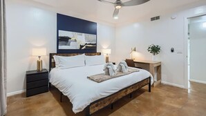 A bedroom with a bed, bedside tables, a ceiling fan, a painting, and a plant.