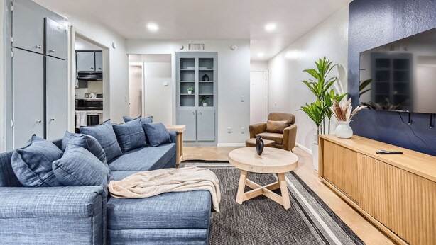 A modern living room with a grey sofa, a wooden coffee table, a brown armchair, and a TV mounted on the wall.
