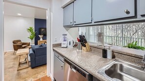 A modern kitchen with grey cabinets, a granite countertop, a built-in dishwasher, and a stainless steel sink.