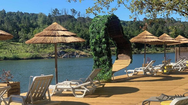 Een houten terras met lounge stoelen en rieten parasols met uitzicht op een meer.