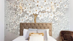 Een slaapkamer met een gestoffeerd hoofdeinde, wit beddengoed en decoratieve witte bloemen aan de muur.