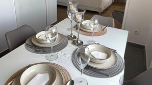 Een eettafel gedekt met borden, glazen en bestek, met een bed en gordijnen op de achtergrond.