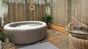 Een hottub in een overdekte buitenruimte met houten wanden, een glazen tafel en rieten meubilair.