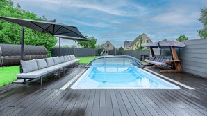 Ein Pool im Freien mit Holzterrasse, Liegestühlen und einer überdachten Sitzgruppe.