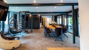 Ein modernes Interieur mit einer Essecke, die einen runden Tisch und Stühle, einen Hängekorbstuhl und eine Treppe umfasst.