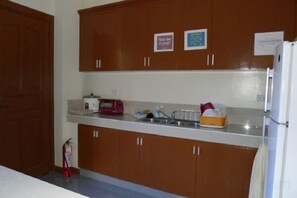 A kitchen with wooden cabinets, a white countertop, a refrigerator, and a fire extinguisher. - Angelic Mansion Palawan (Puerto Princesa)