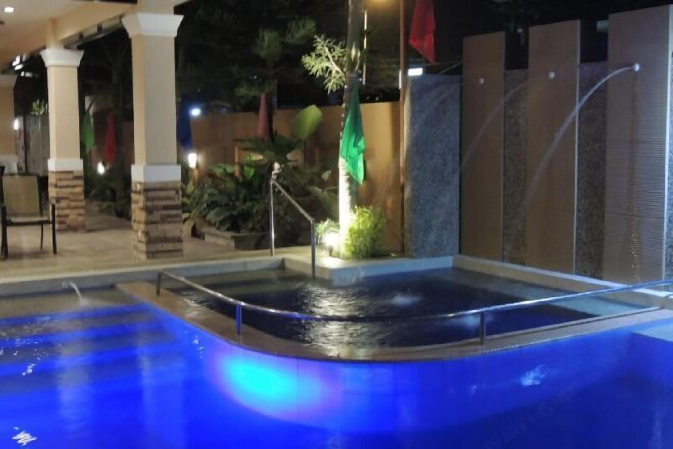 An indoor swimming pool with a water feature, surrounded by a covered area with seating and plants.
