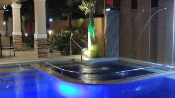 An indoor swimming pool with a water feature, surrounded by a covered area with seating and plants.