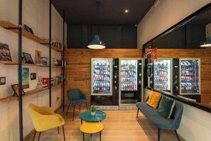 A cozy interior with wooden walls, a sofa, two chairs, a small table, and vending machines. - Rodamón Barcelona Hostel (Barcelona)