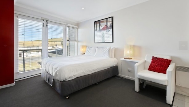 A modern hotel room with a large bed, a chair, a bedside table, and a window with blinds. - White Crystal 112- ski-in ski-out (Mount Hotham)