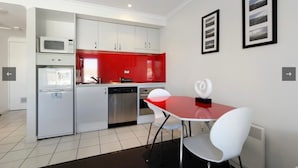 A modern kitchen with white cabinets, a red backsplash, and stainless steel appliances. There is a dining area with a red table and white chairs. - White Crystal 112- ski-in ski-out (Mount Hotham)