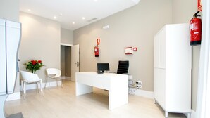 Un ufficio moderno con scrivania bianca, due sedie, un computer e un estintore a parete.