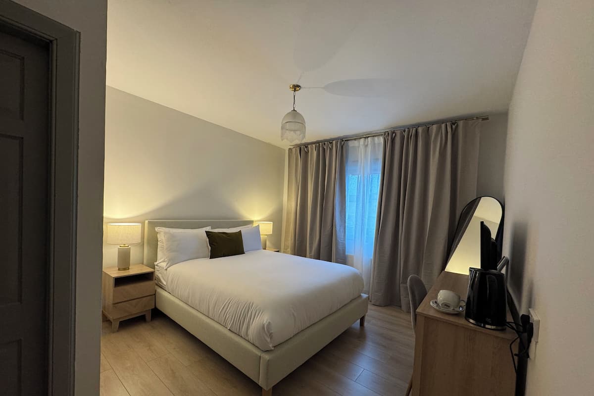 Un dormitorio con cama, lámparas de noche, mesita de noche, espejo y ventana con cortinas.