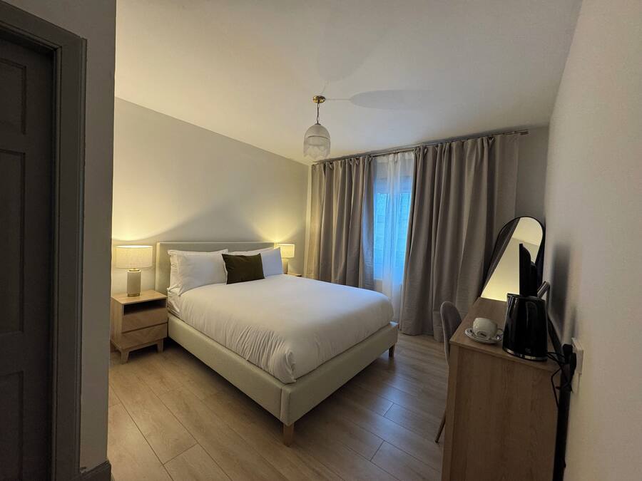 A bedroom with a bed, bedside lamps, a nightstand, a mirror, and a window with curtains.