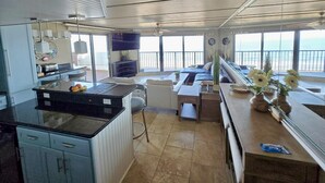 Una cocina amplia con una isla grande, un comedor con vistas al océano y una sala de estar con sofá y televisor.