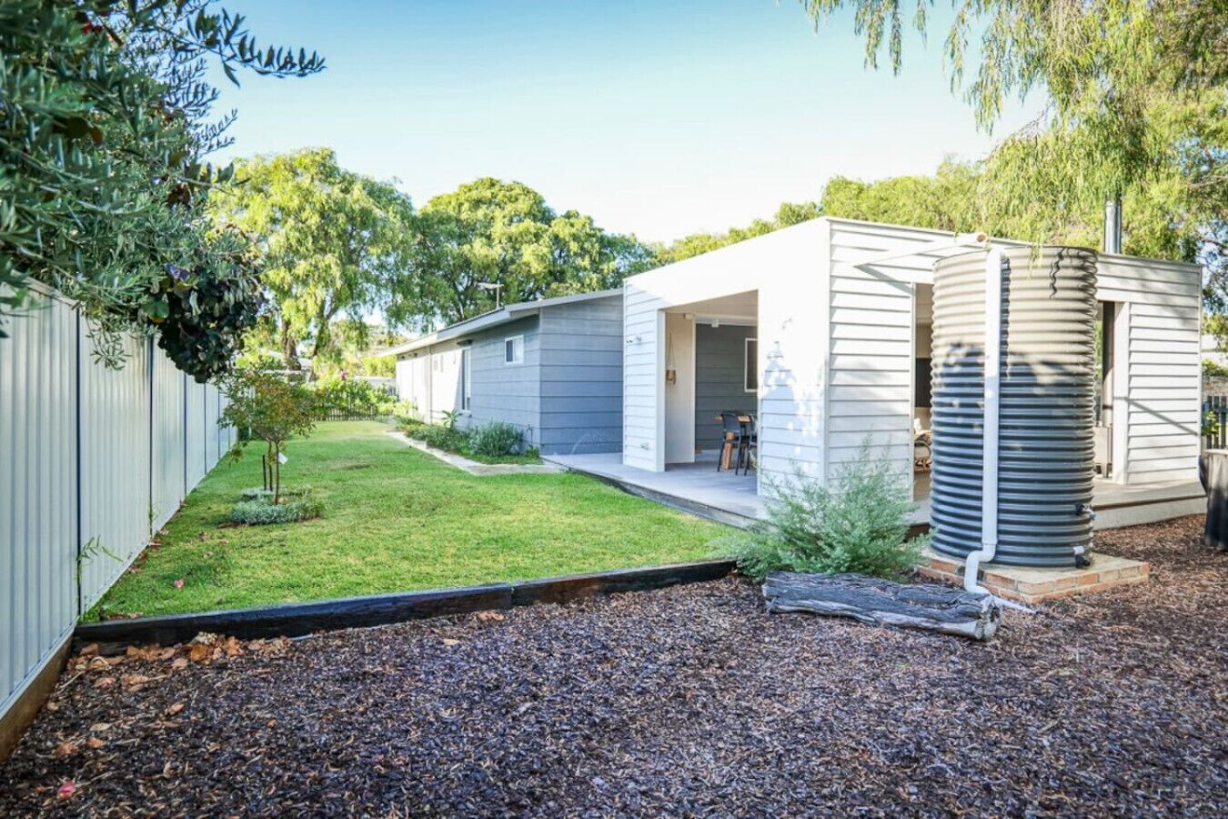Una casa moderna a un piano con veranda coperta, un piccolo giardino e un serbatoio d'acqua di grandi dimensioni.