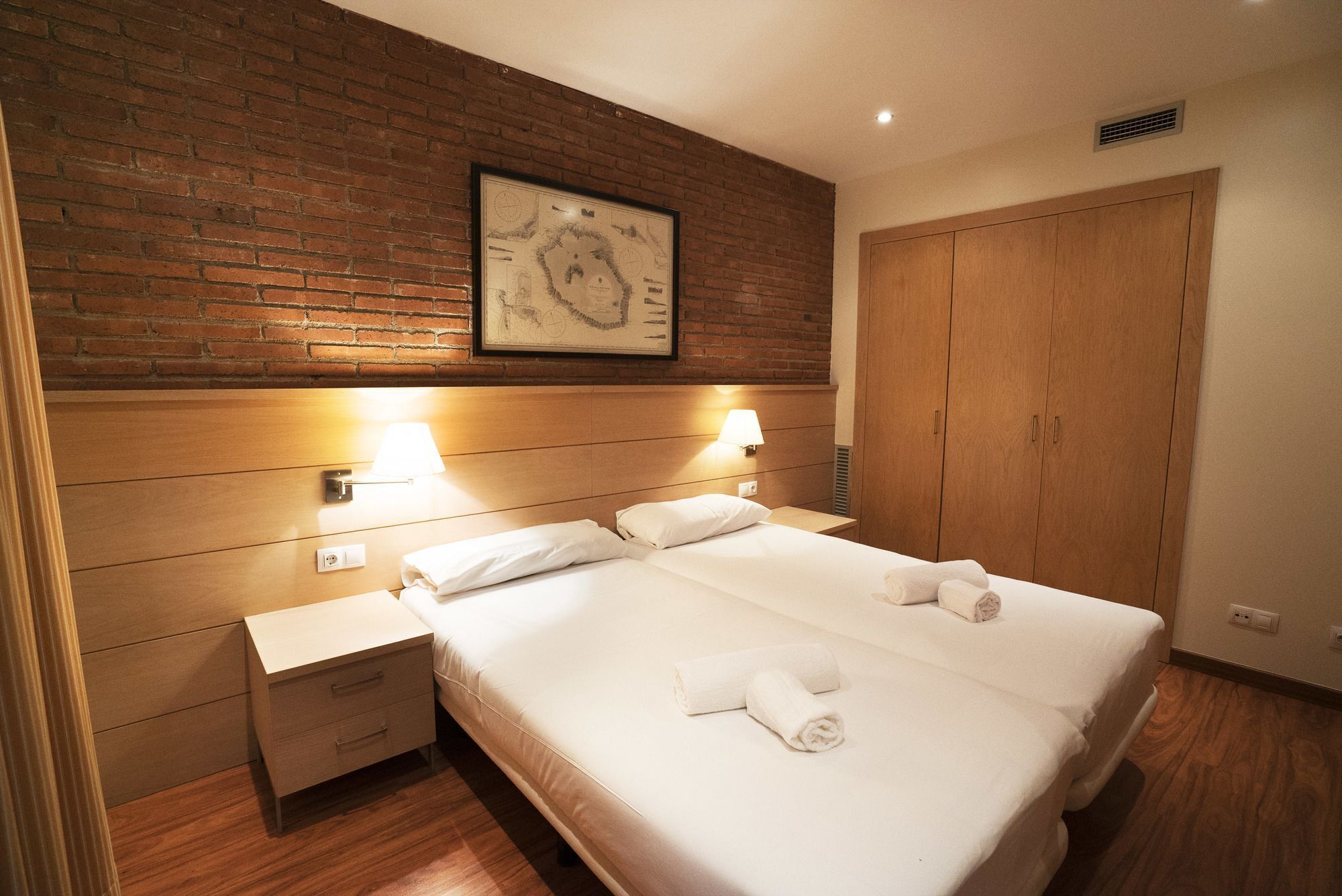 Ett hotellrum med en stor säng, två sängbord, en garderob i trä och en tegelvägg med en inramad karta.