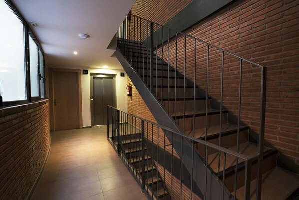 A modern interior with a brick wall, a metal staircase, and a door leading to an elevator. - Serennia Cest Apartamentos Arc De Triomf (Barcelona)