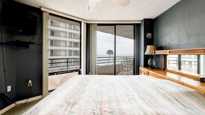 Une chambre dotée d’un grand lit, d’un ventilateur de plafond, d’un téléviseur fixé au mur et offrant une vue sur l’océan grâce à une porte-fenêtre coulissante.