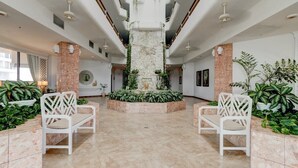 Un hall d’entrée spacieux avec une fontaine centrale, des chaises blanches et une végétation luxuriante.