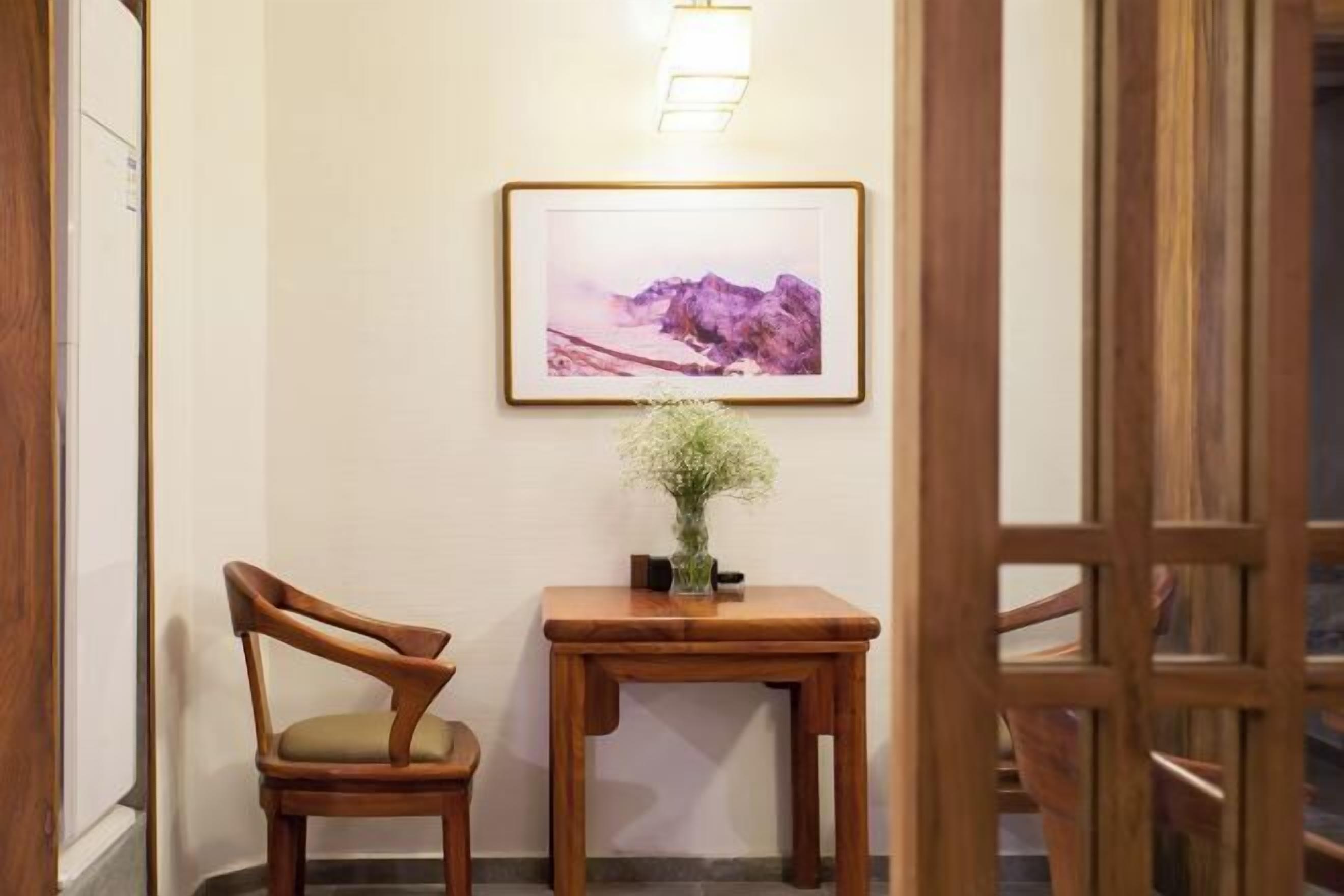 A wooden chair and table in a hallway with a framed picture on the wall.