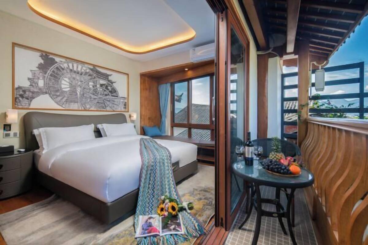 A hotel room with a large bed, a balcony with a table and chairs, and a view of the city.