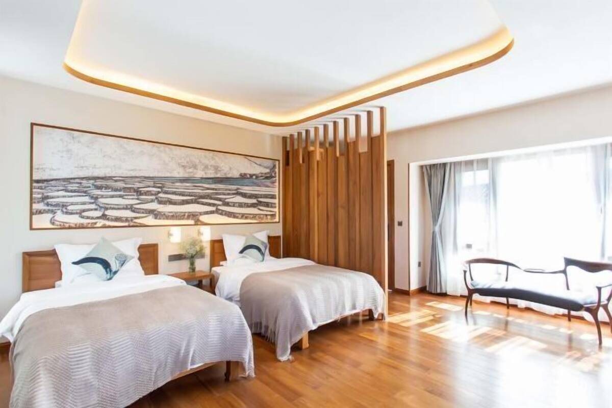 A modern hotel room with two beds, a large painting, a wooden partition, and a view of the outdoors.