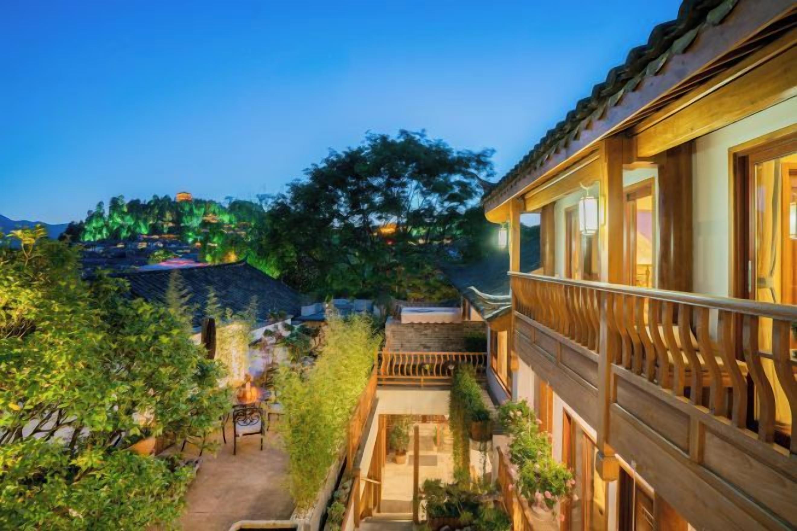 A traditional building with a balcony, a pathway leading to a door, and a view of a hill with lights.