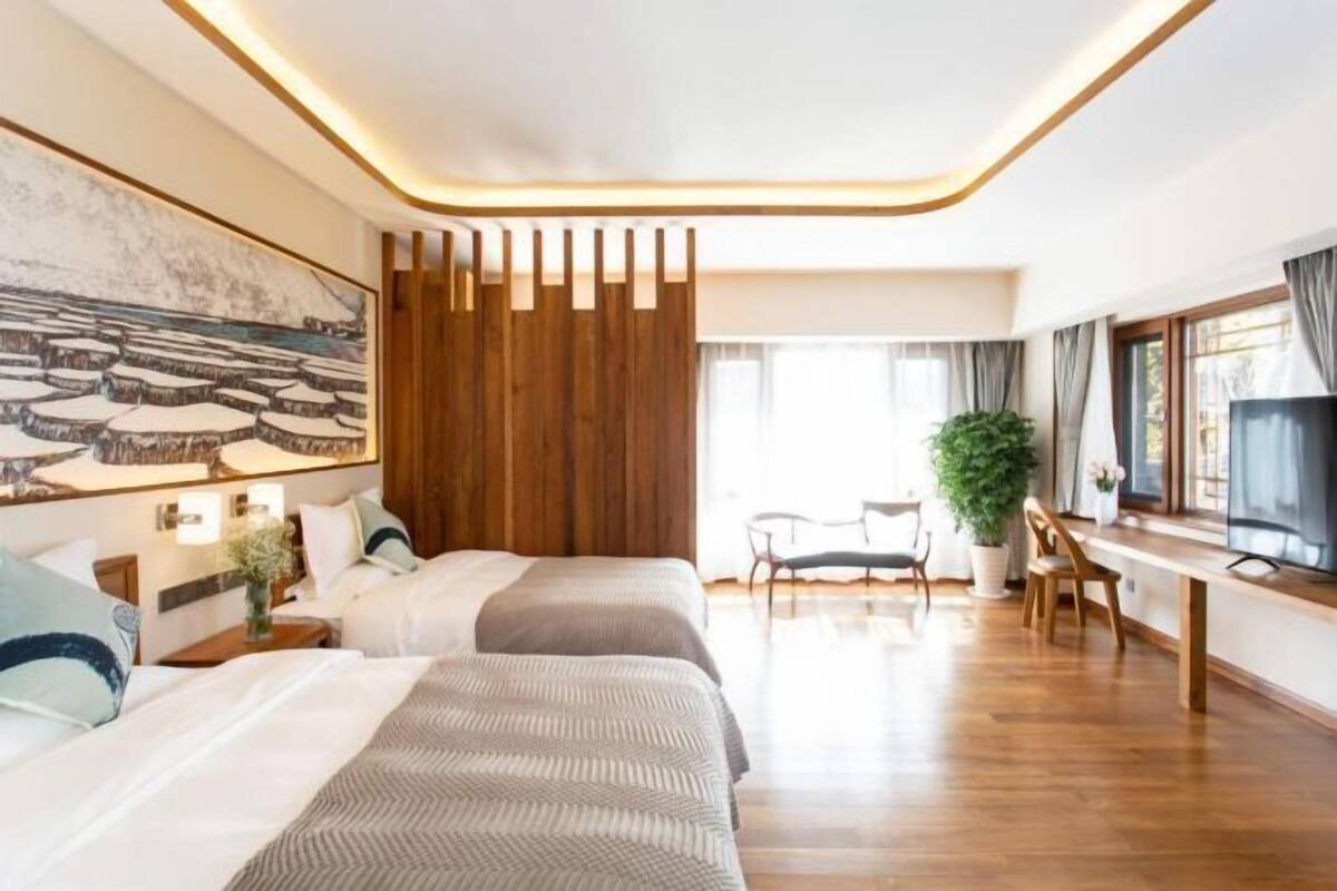 A hotel room with two beds, a desk, a chair, a TV, and a large window.