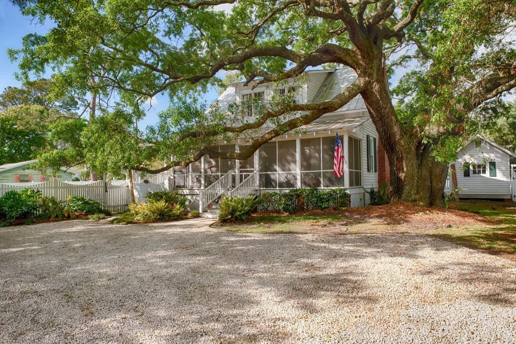 Une maison avec un grand arbre devant, une allée en gravier et une clôture blanche en bois.