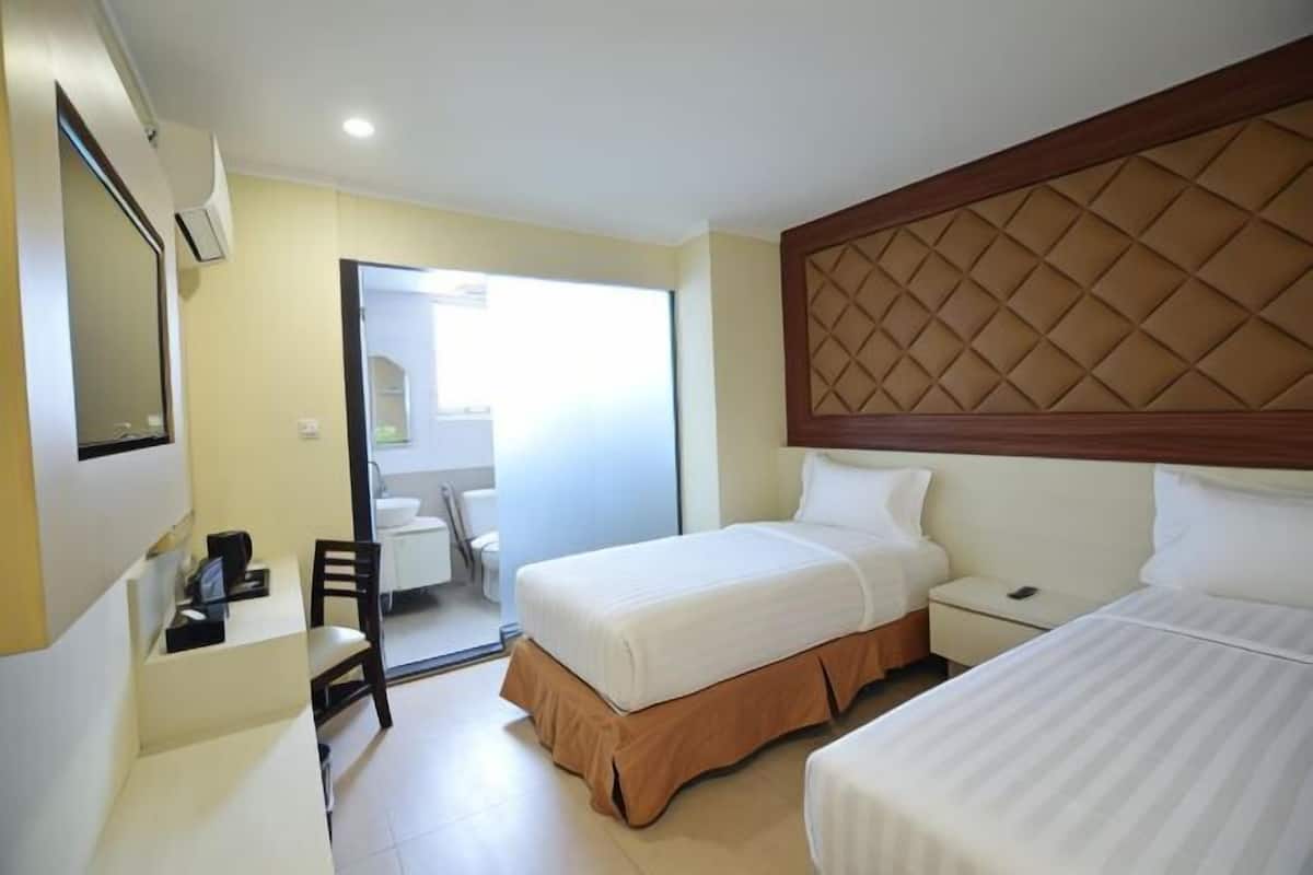 Une chambre d’hôtel avec deux lits, un bureau, une chaise, un miroir et une salle de bain visible à travers une porte ouverte.