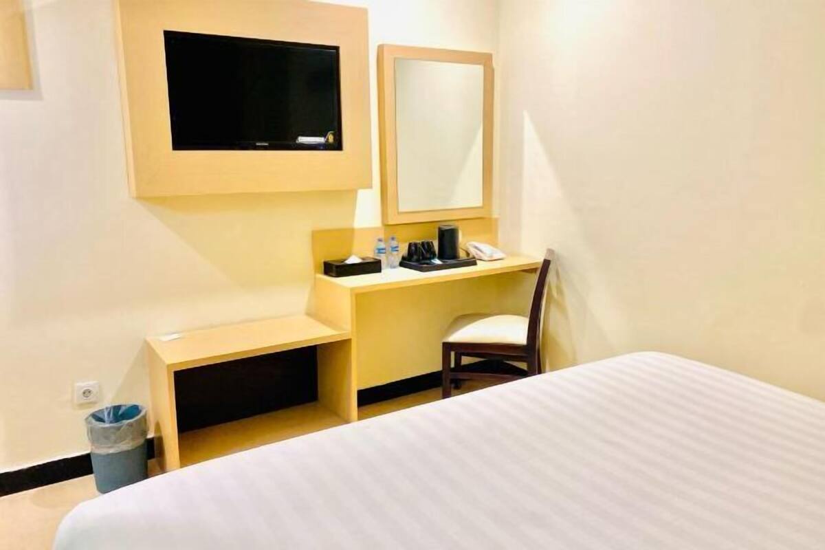 Une chambre d’hôtel comprenant un lit, un bureau avec une chaise, une télévision, un miroir et une poubelle.