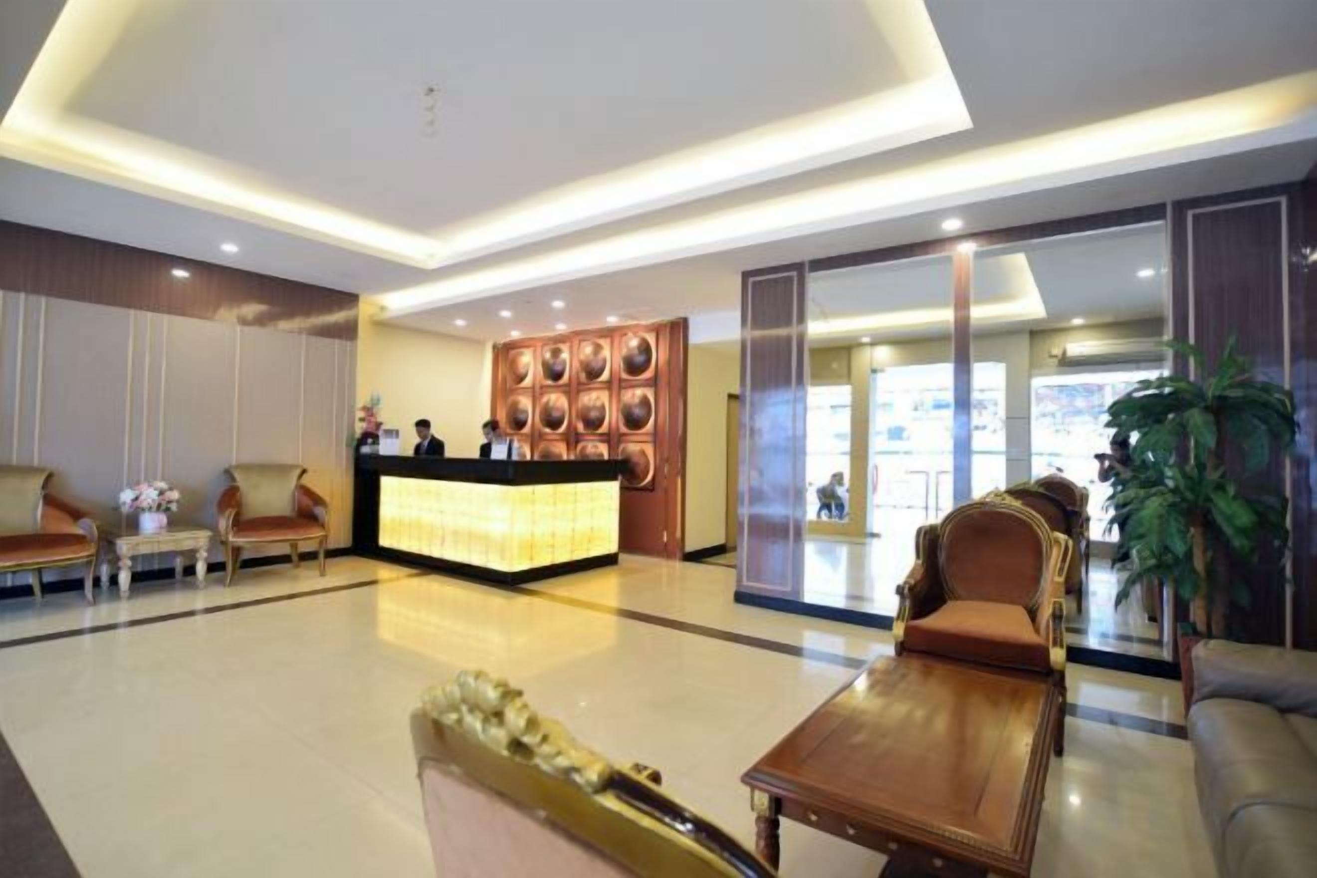 A hotel lobby with a reception desk, seating area, and a large plant.