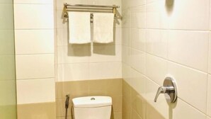 Un baño con azulejos blancos, inodoro, ducha y toallero con dos toallas.