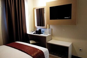 Ein Hotelzimmer mit einem Bett, einem Schreibtisch mit Telefon, einem an der Wand befestigten Fernseher und einer kleinen Sitzecke.