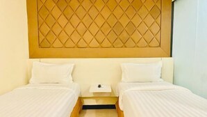 Habitación de hotel con dos camas individuales, una mesita de noche pequeña y un cabecero con diseño de rombos.