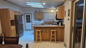 A kitchen with wooden cabinets, a central island with stools, a refrigerator, and a dining table with chairs. - Trails and fishing paradise  (Nashwauk)