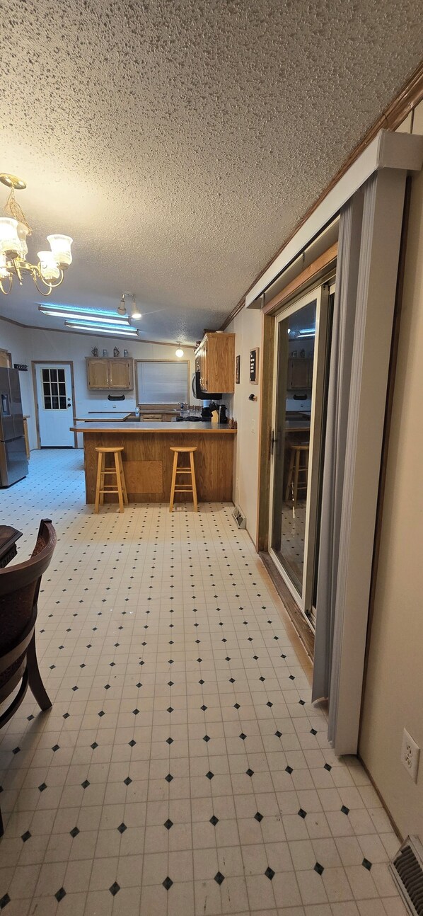 A kitchen with a central island, wooden stools, a refrigerator, and a sliding glass door leading to a balcony.