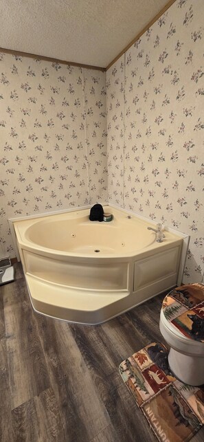 A bathroom with a freestanding bathtub, wooden flooring, and floral wallpaper.