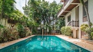 A rectangular swimming pool with clear blue water, surrounded by lush tropical vegetation and a building with balconies. - Orchid Pool Villa Lavish Villa in Perfect Location (Phuket)