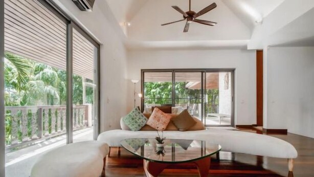 A spacious room with a large window, a ceiling fan, a sofa, and a glass coffee table. - Orchid Pool Villa Lavish Villa in Perfect Location (Phuket)