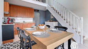 A modern kitchen with wooden cabinets, a dining table set with plates and glasses, and a staircase leading to an upper level. - Marine calm - QUIBERON (QUIBERON)