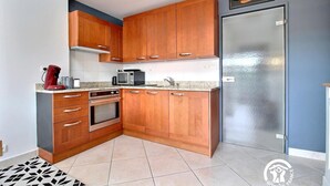 A compact kitchen with wooden cabinets, a stainless steel refrigerator, and a microwave. - Marine calm - QUIBERON (QUIBERON)